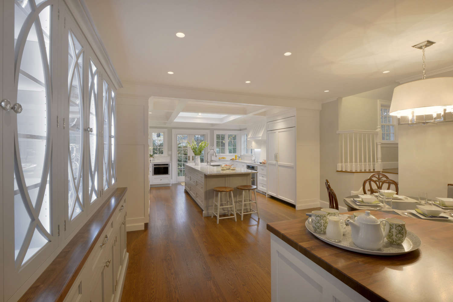 U-shaped Larchmont kitchen features a mix of Rutt Handcrafted cabinets and Rutt Regency cabinets. Kitchen has a large island, hutch, banquet area, white painted cabinets and natural oak flooring, and opens up into living room. Designed by Fabrice Garson of Bilotta Kitchens.