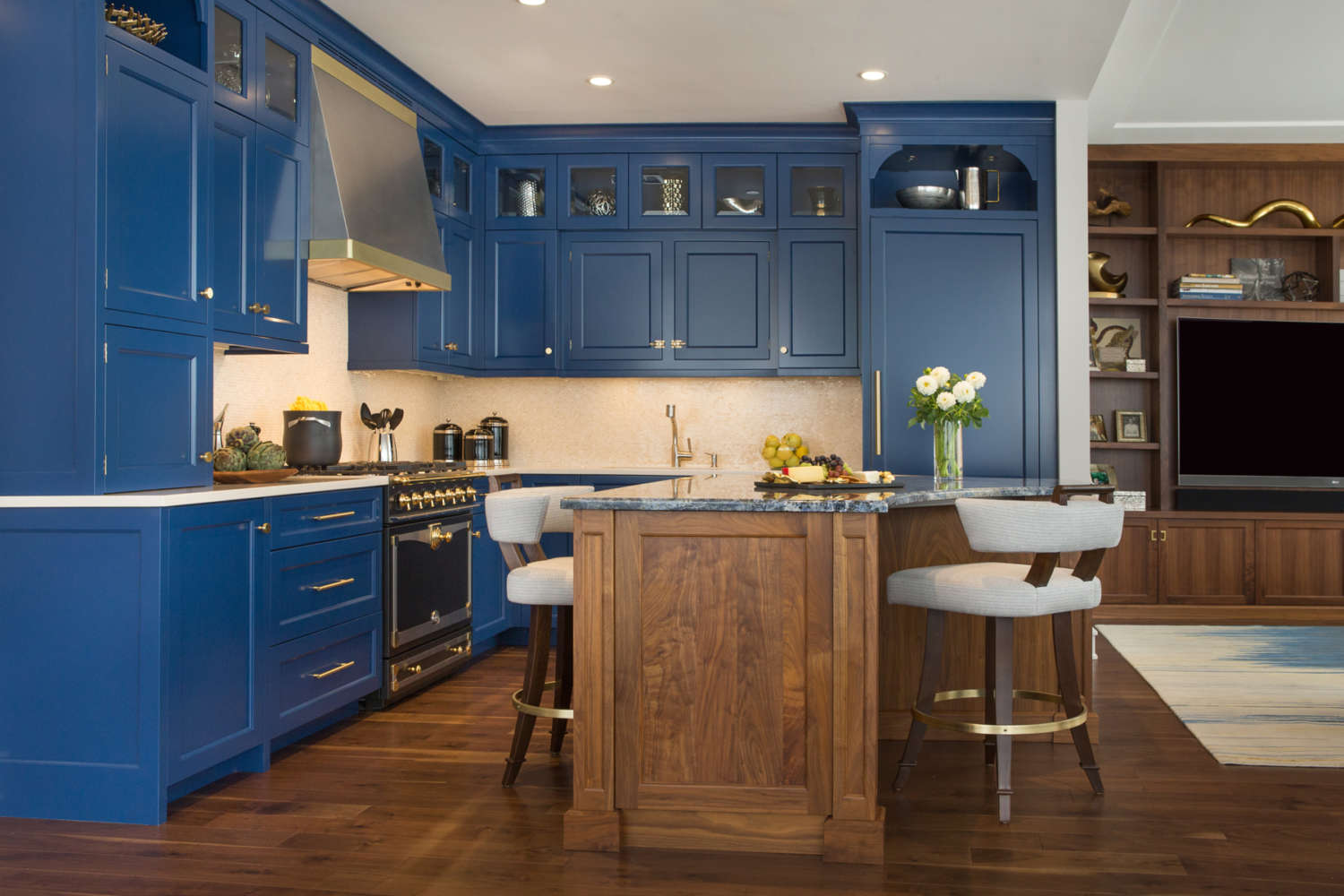 L-shaped kitchen with blue painted custom kitchen cabinets with shaker style doors. Walnut island with seating. Bilotta custom cabinets and shelving in walnut with mid-century modern vibe in adjacent living room area. Designed by Jeni Spaeth of Bilotta Kitchens.