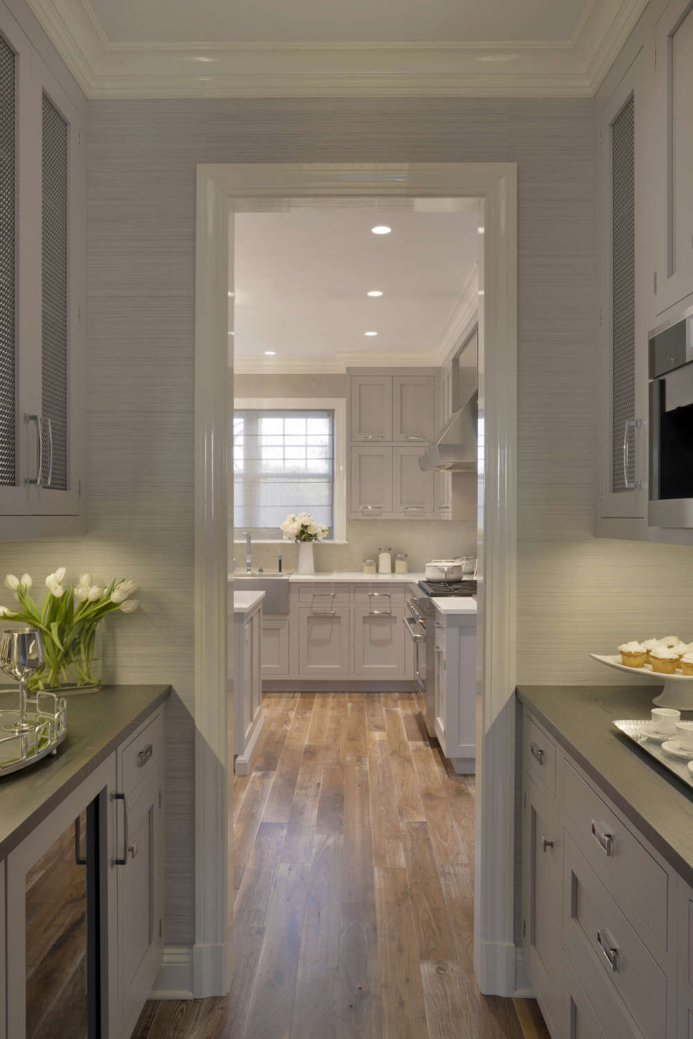 Butler's pantry features light grey painted shaker style Biotta cabinetry with metal door inserts, grey walls and espresso countertops. Pantry opens into an expansive kitchen. Design by Randy O'Kane, CKD, of Bilotta kitchens.