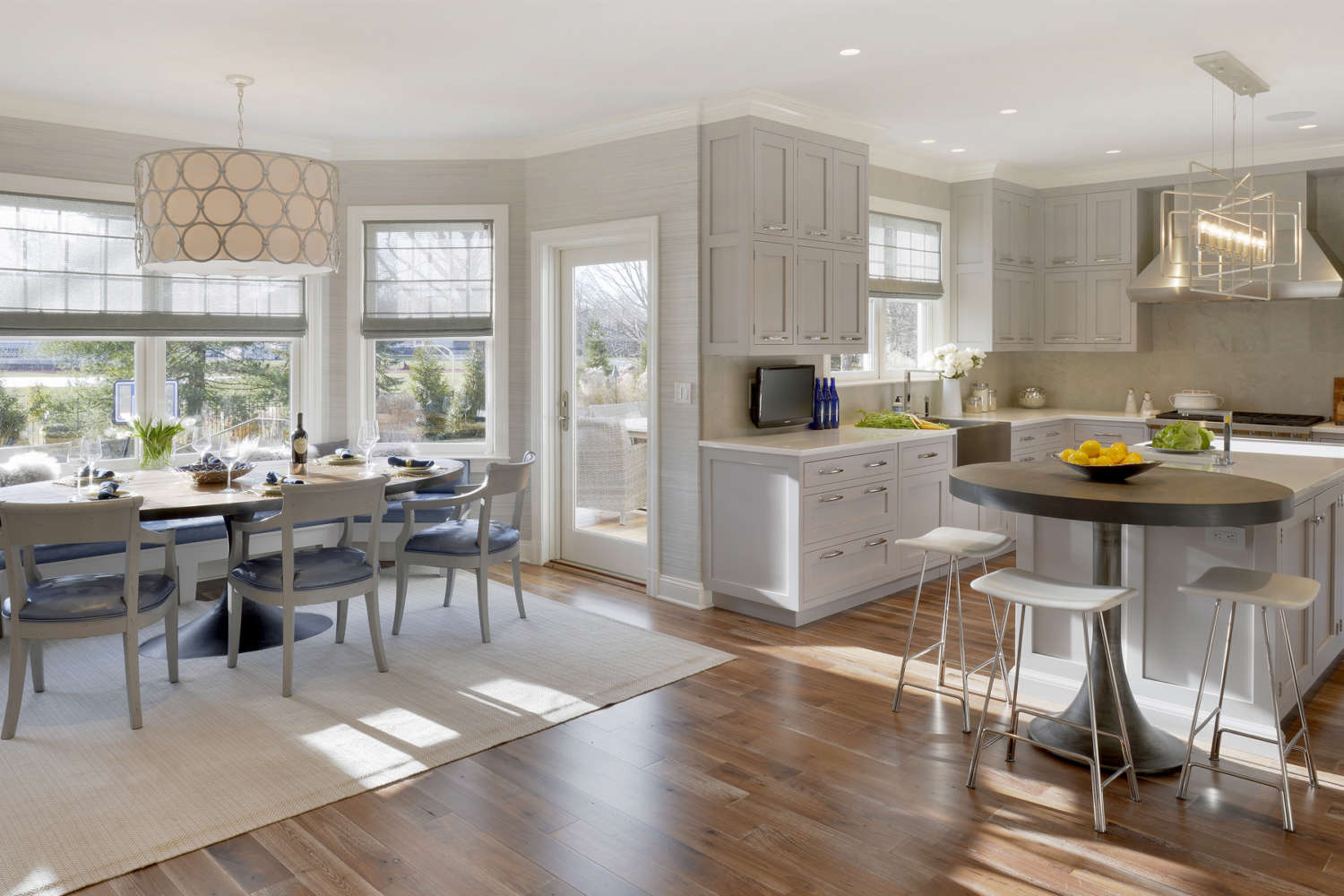 Kitchen features oak flooring, pale grey walls, white quartz countertops, custom shaker style double tiered Bilotta cabinetry in a mix of rift cut white oak and white painted finish, and a center island with adjoining table with seating.