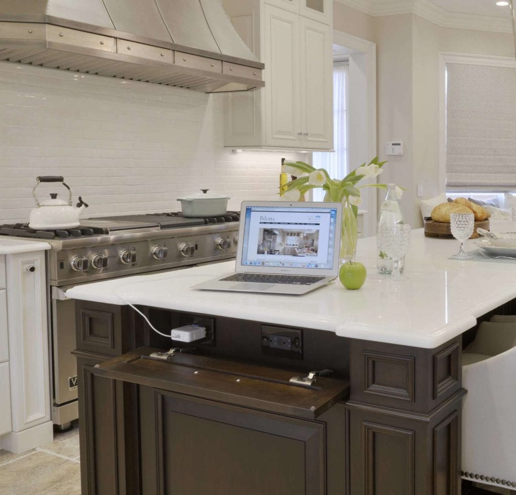 Classic white and cherry kitchen with hidden outlets and laptop on island.