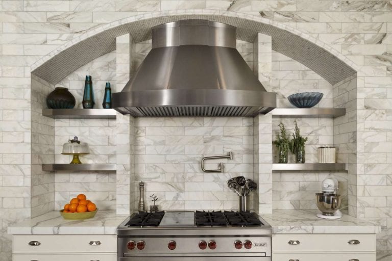Custom arch-shaped marble hearth features open stainless shelving and oversized stainless hood.