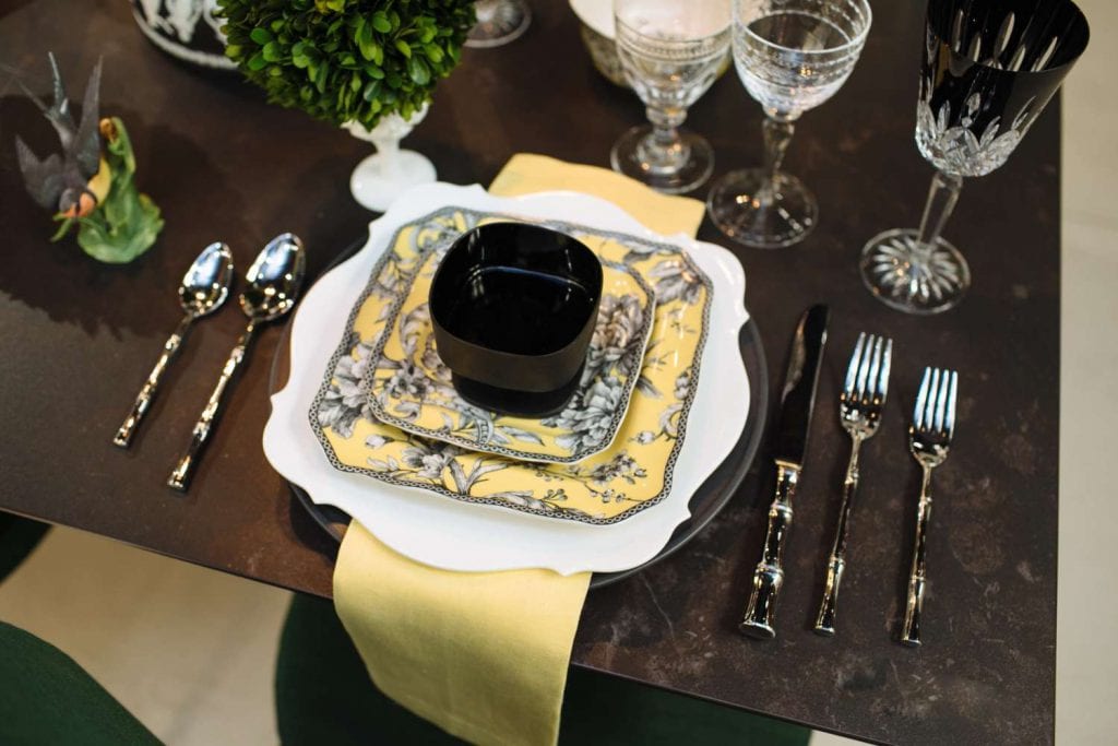  toile-style place setting of black florals and birds on yellow, called Adelaide yellow, by 222 Fifth coupled with yellow napkins and bamboo shaped flatware