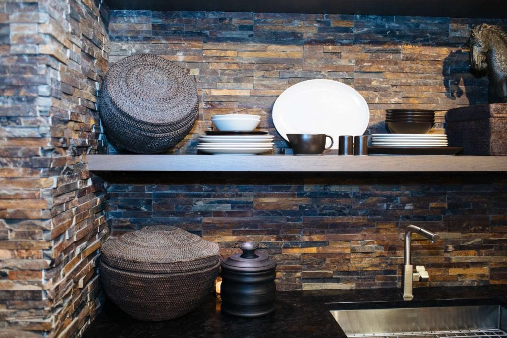 rice baskets, dishes and antiques on open oak shelves mounted on a jagged stone wall 