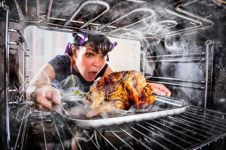 A frazzled home cook pulls a smoking, burnt turkey from the oven.