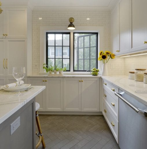 Traditional kitchen with gray herringbone tile floor, white custom cabinets, brass hardware and black gloss accents.