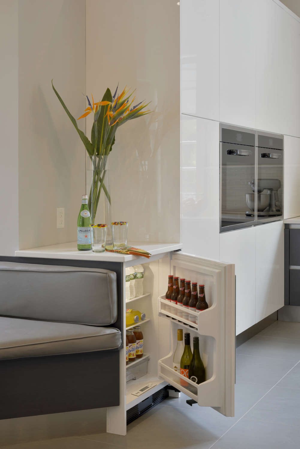 Beverage fridge is built into a kitchen and banquette design and topped with white marble counter.