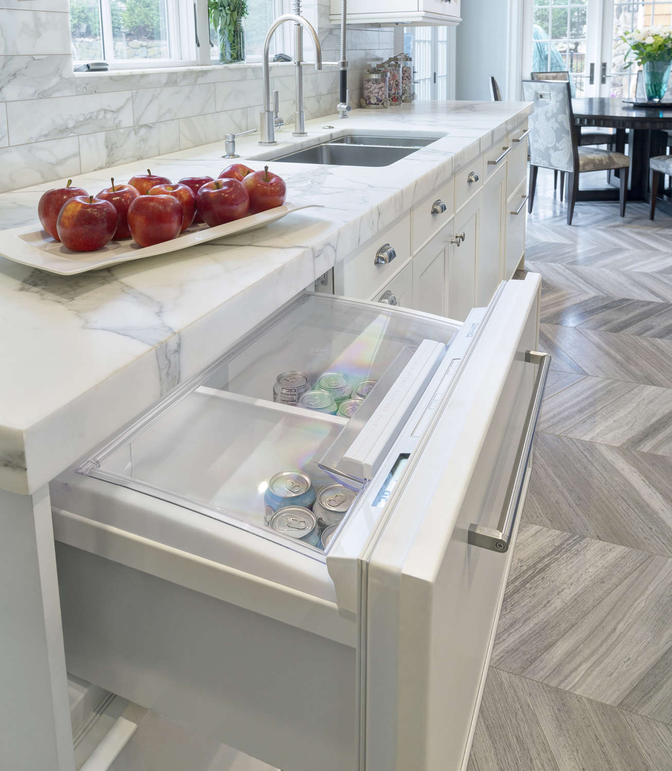 Kitchen features wood herringbone flooring and white bilotta cabinetry with under-counter beverage drawer and stainless hardware.