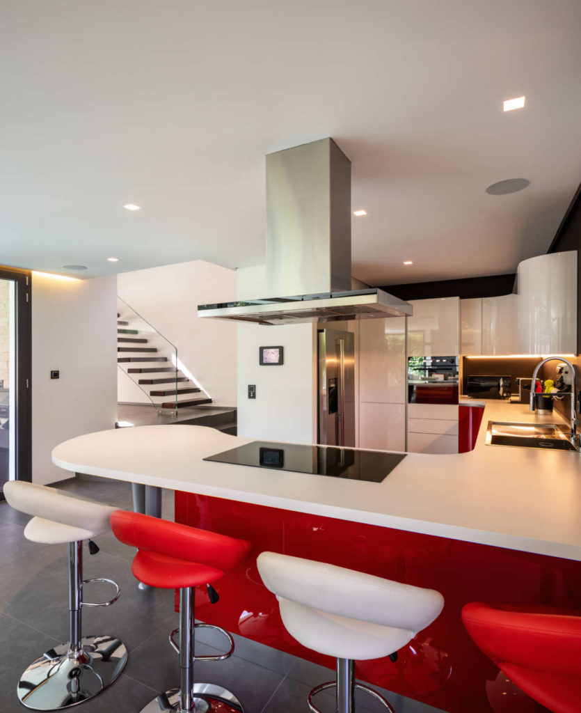 Contemporary kitchen with white quartz-topped cherry red island, red and white leather stools and stainless accents.