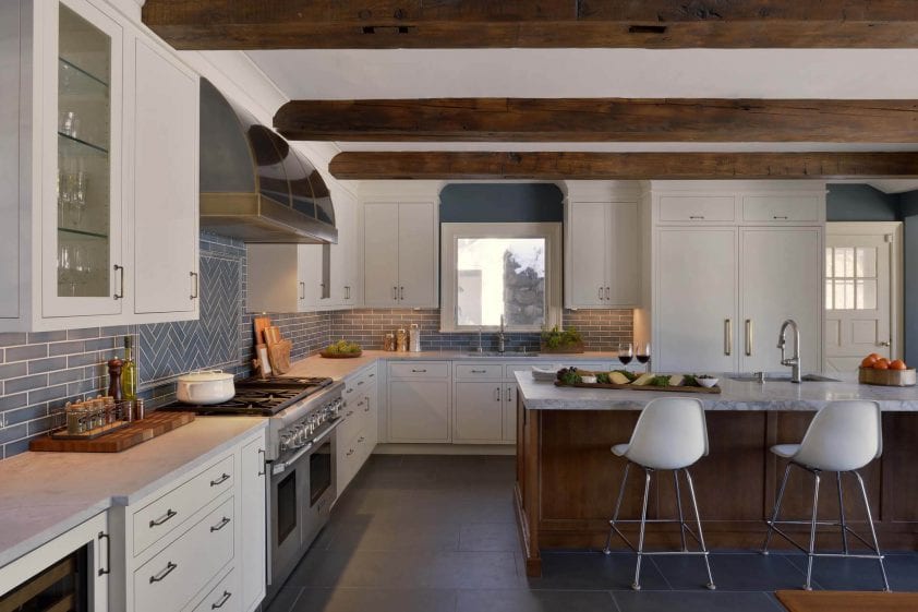 Exposed beam kitchen features white Bilotta Signature cabinetry with German antique glass inserts and glazed blue tile backsplash.