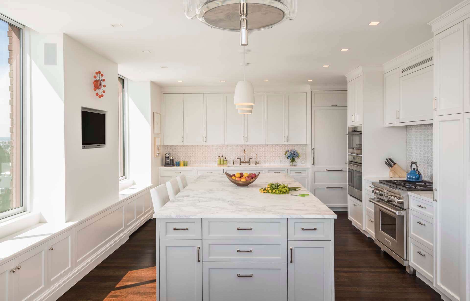 Classic all-white kitchen features Rutt cabinetry with brushed stainless hardware, marble countertops and a skyline view.