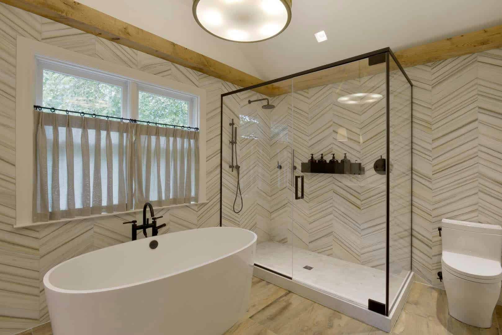 Custom classic bathroom features dramatic Helsinki Chevron Silver Dusk walls, glass enclosed shower and a soaking tub.