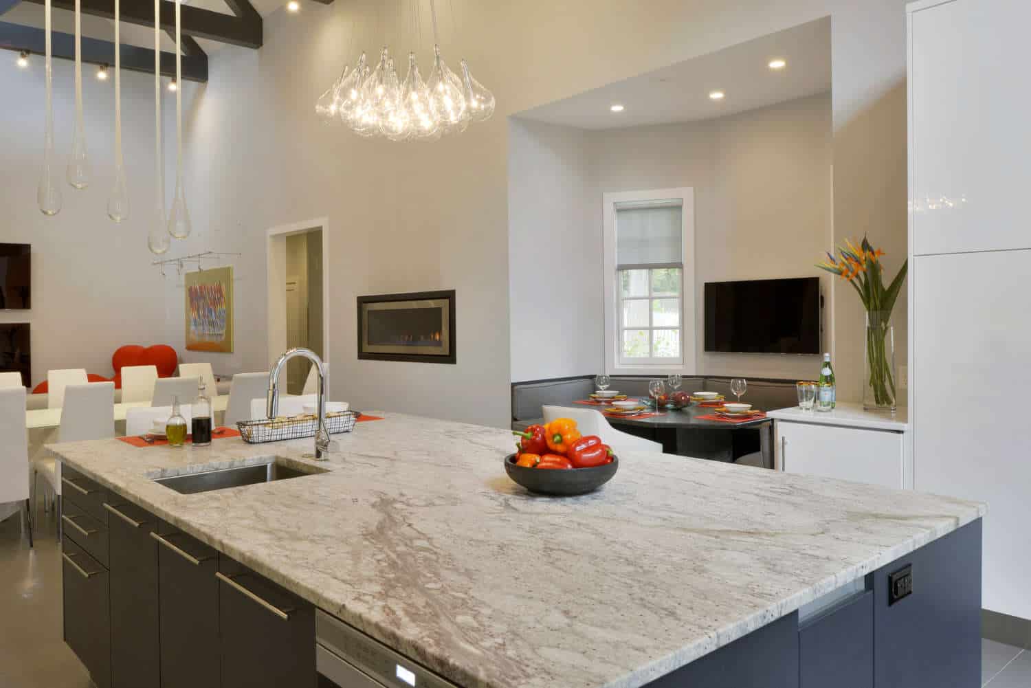 Thunder White granite-topped grey-stained oak island with channel hardware is lit by a dramatic glass pendant chandelier