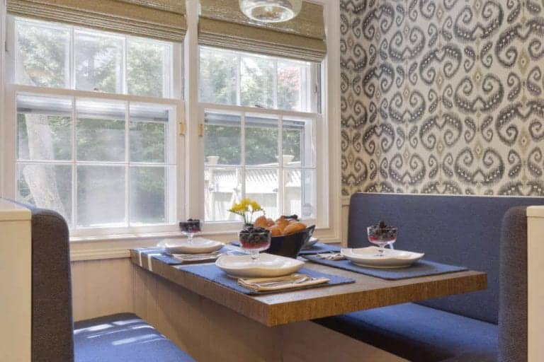 Cozy custom banquette features navy cushions, elegant damask wallpaper and glass cylinder pendant light.