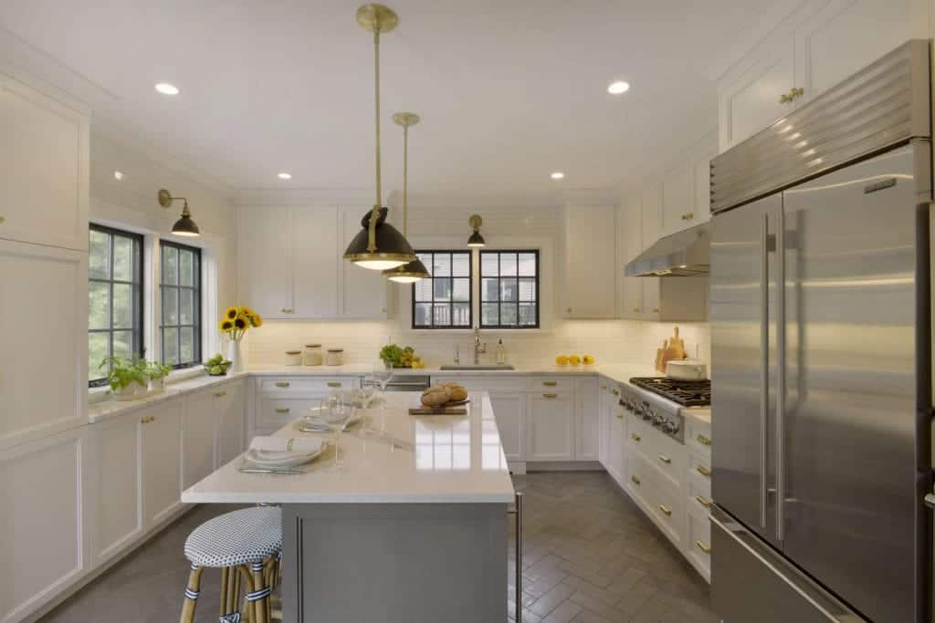 Kitchen features white Caesarstone topped white NAC cabinetry, herringbone floor tile. and black and brass accents.