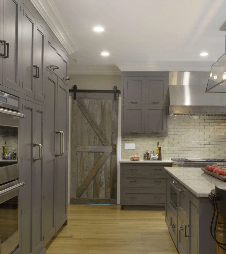 Country kitchen features grey Bilotta cabinetry, White Macambas Caesarstone countertops and a reclaimed barn door.