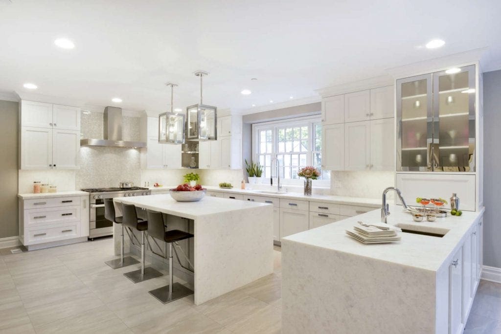 All-white kitchen with Bilotta cabinetry features custom island with silver pendant lights and adjacent dining area.