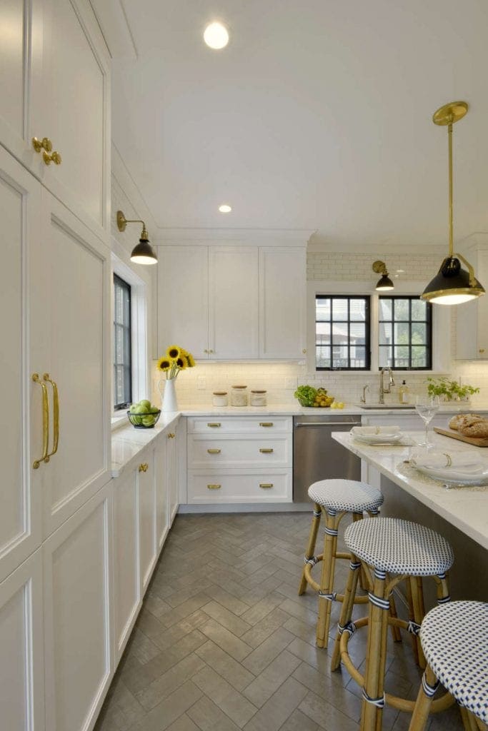 Kitchen features white cabinetry with brass hardware and herringbone tile flooring.