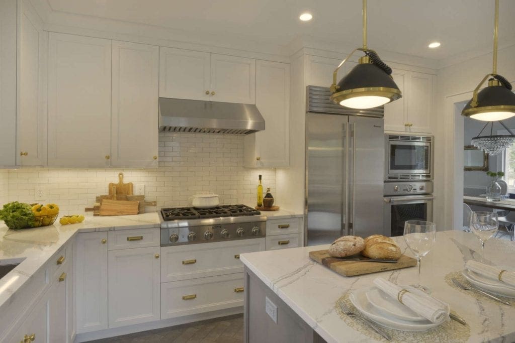 White kitchen features glazed white subway tile backsplash and brass accents