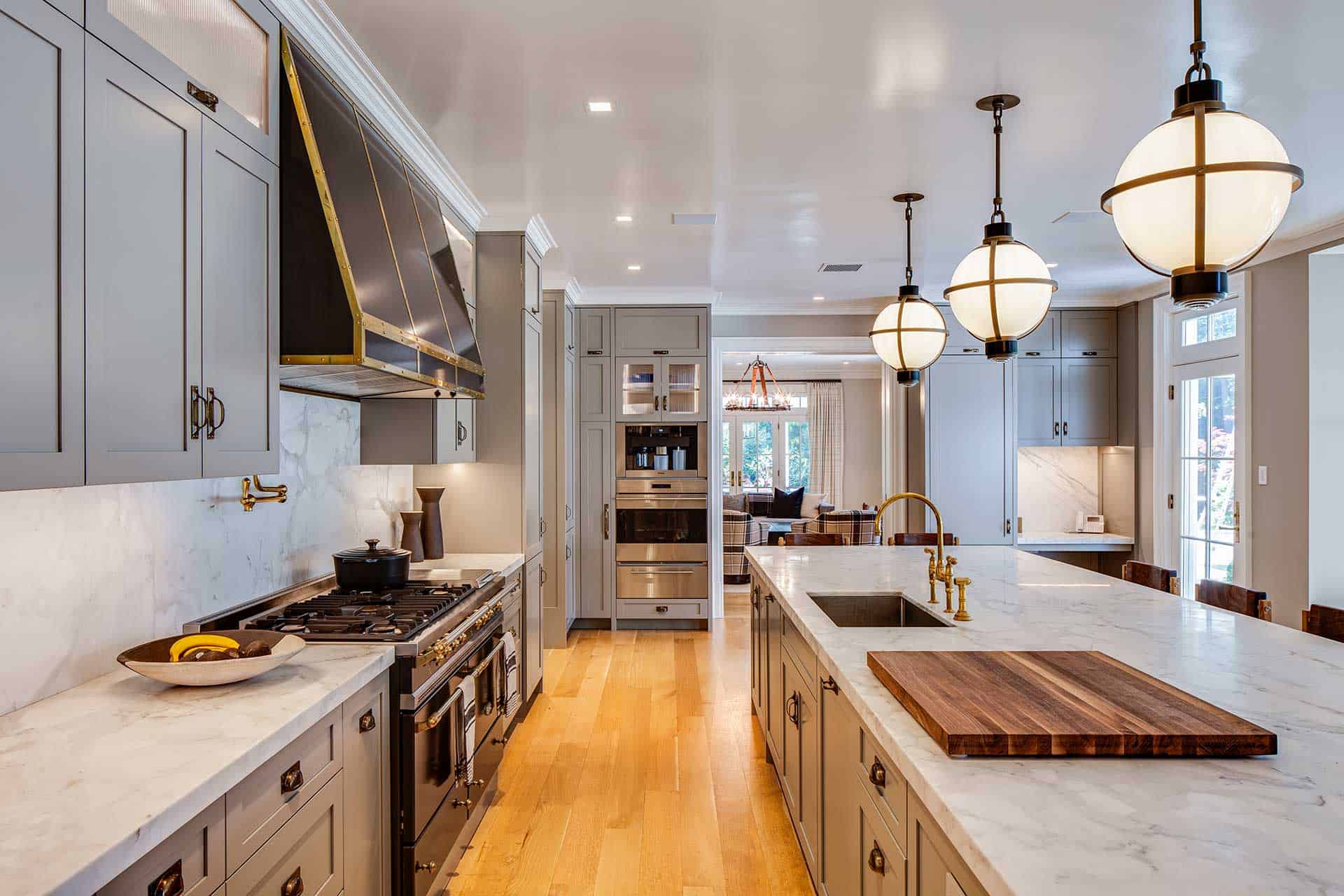 Brass-wrapped globe pendants light the large, marble topped island of this expansive grey-painted Bilotta kitchen.