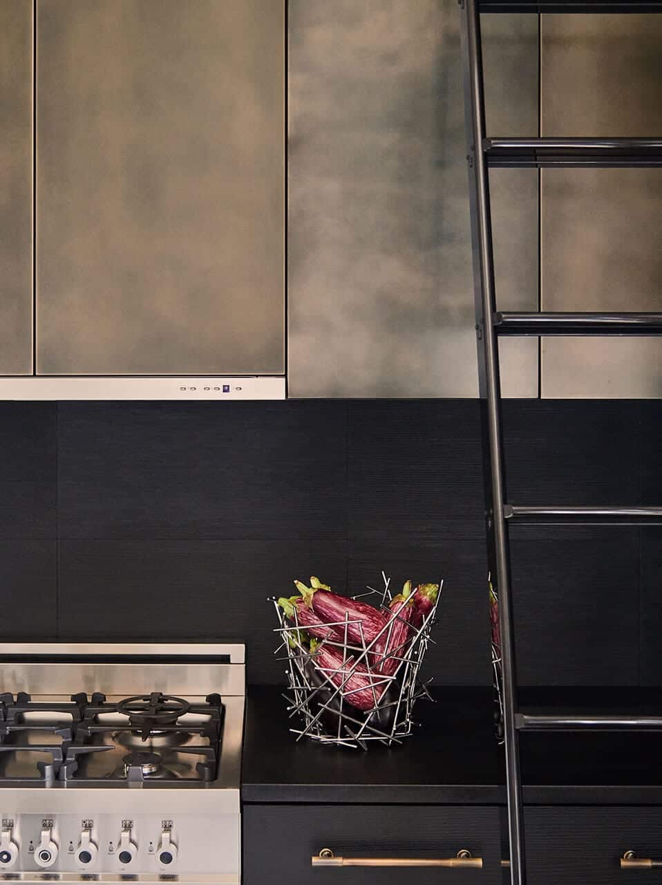 Chic contemporary kitchen with dark, moody finishes utilizes a black lacquer rolling ladder to reach the cabinets.