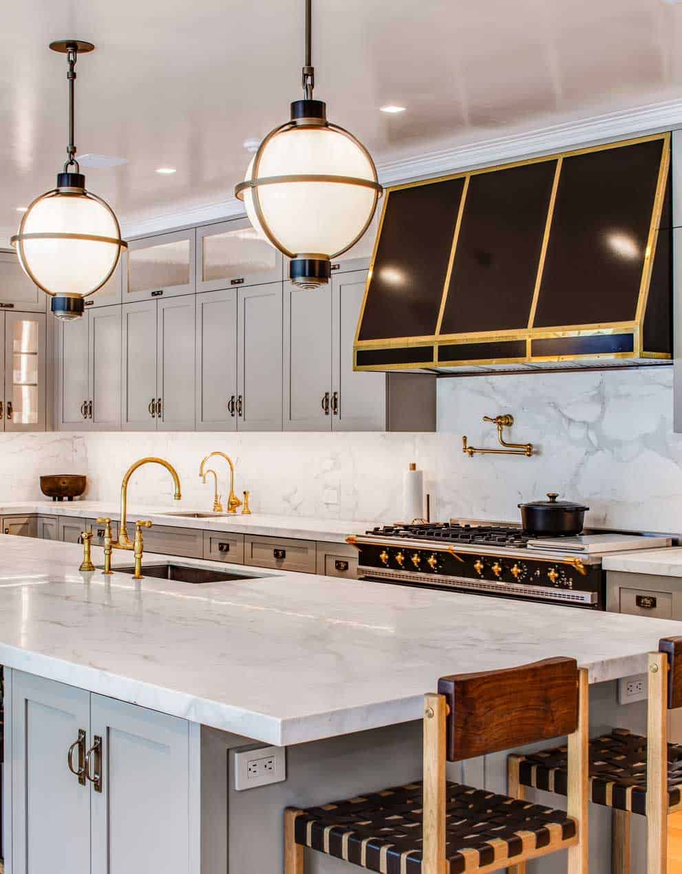 Brass-wrapped globe pendants light the large, marble topped island of a European-inspired kitchen.
