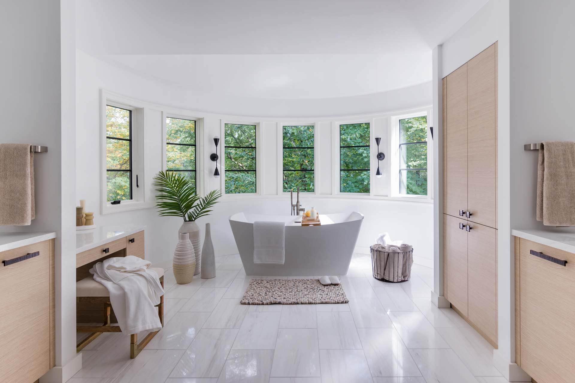 Contemporary spa bathroom features a large bay of windows, pale oak cabinetry, light dolomite tiles and soaking tub.