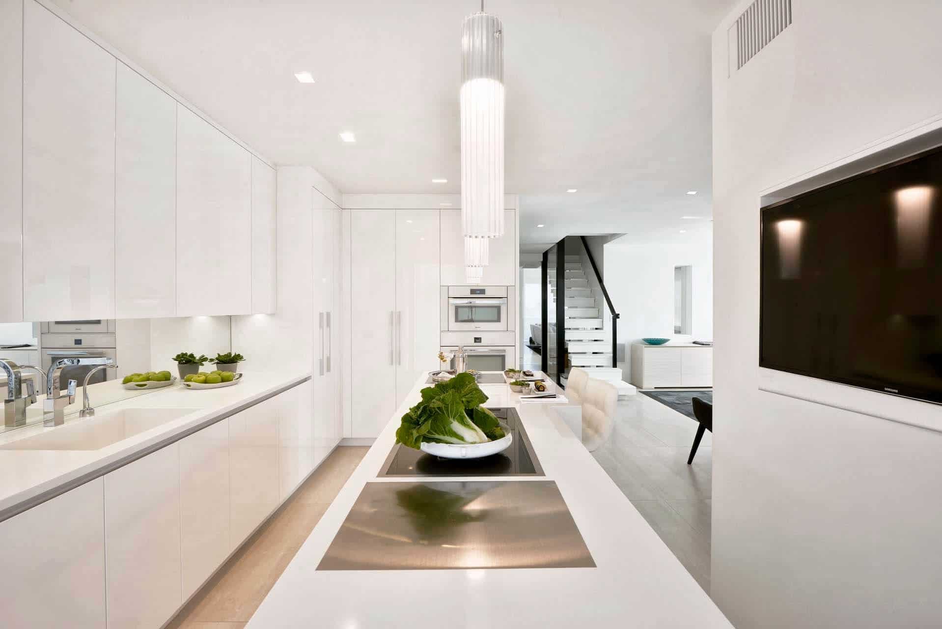 Contemporary all-white kitchen features full-length island, dramatic pendant lights and pure white gloss Artcraft cabinetry.