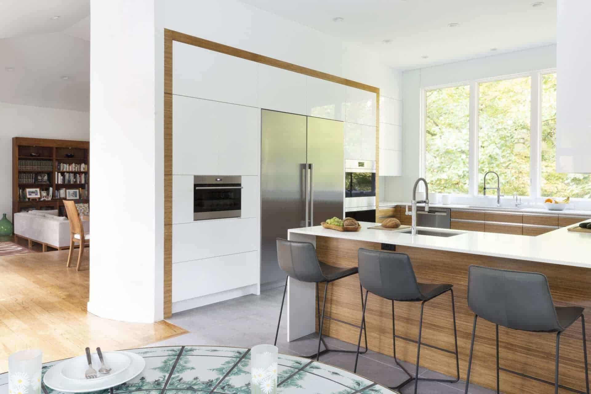 Modern kitchen mixes white and bamboo. NAC cabinetry with stainless hardware. L-shaped island has Caesarstone waterfall countertop.
