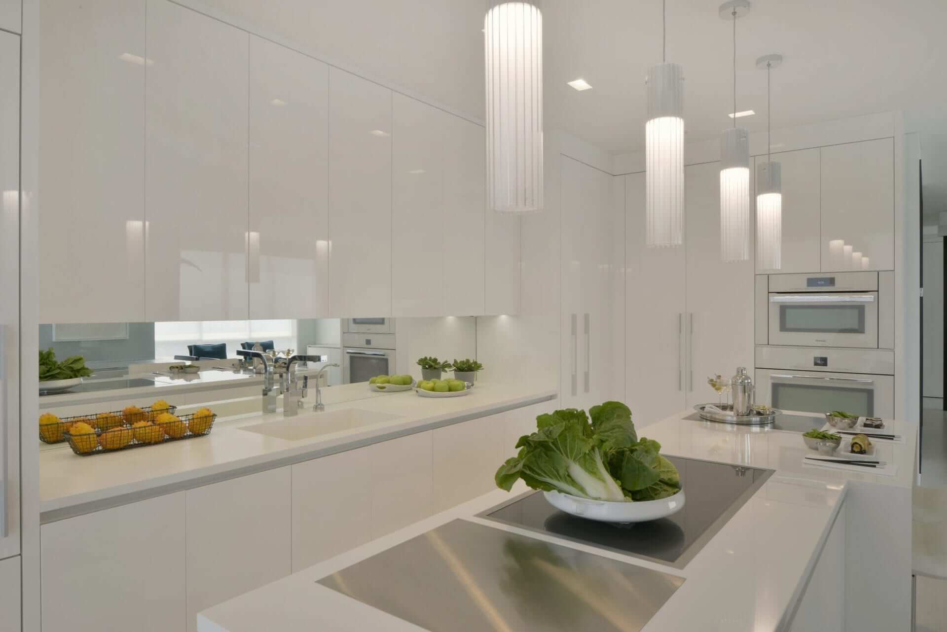 Custom island features white Corian top with waterfall edge, white leather stools and white glass cylinder pendant lights.