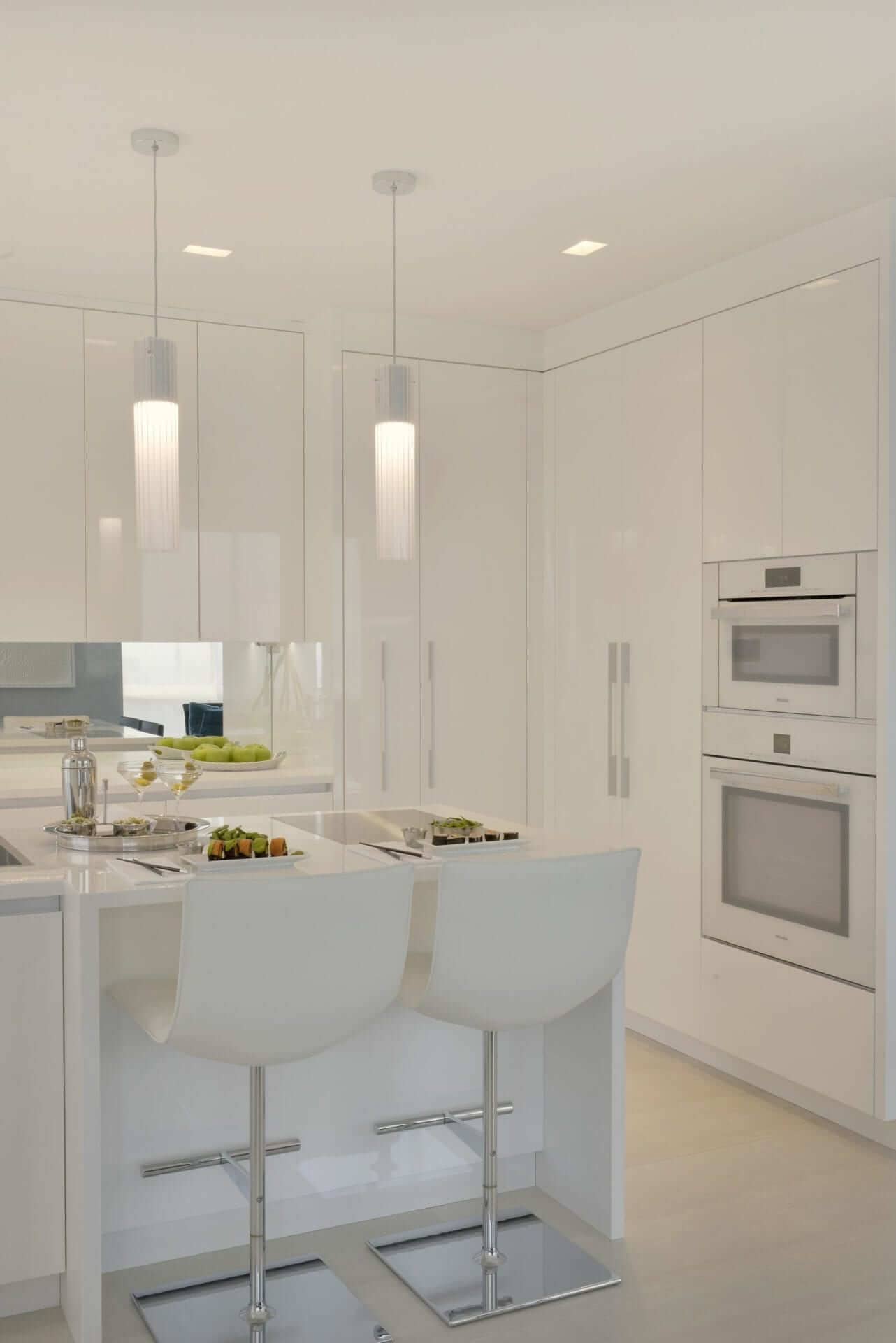 Island seating area in contemporary all-white kitchen features dramatic pendant lights and white Corian countertop with waterfall edge.