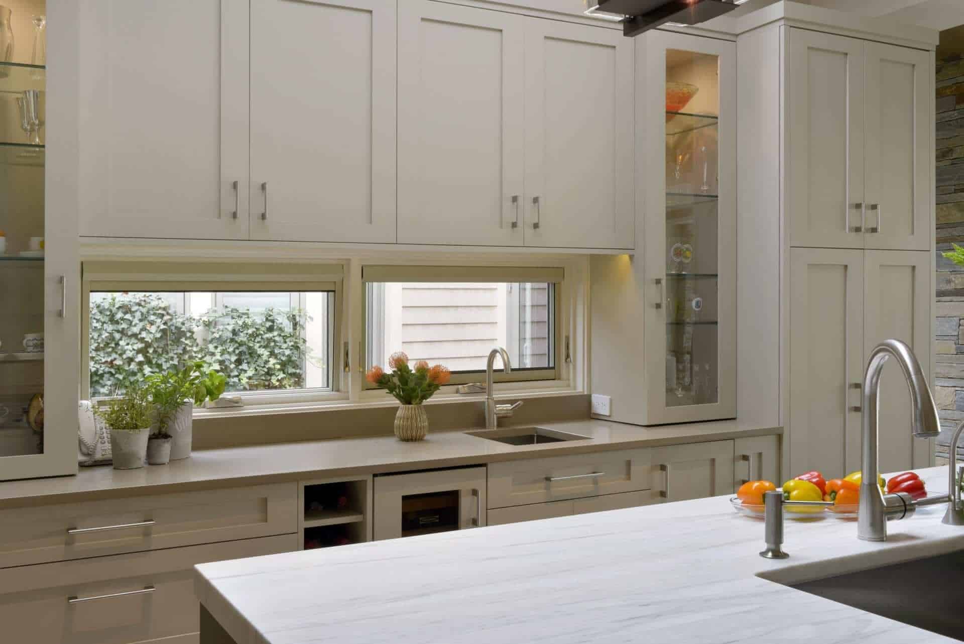 Contemporary kitchen features Rutt cabinetry in Stone with a mix of inset doors and glass front lit cabinetry.