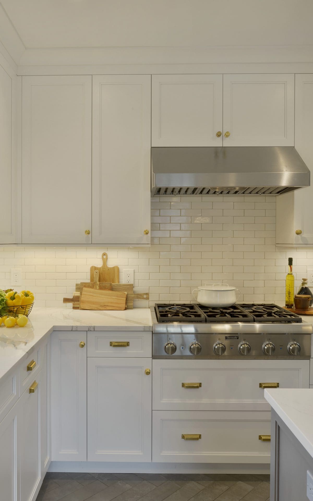 Classic kitchen features white Bilotta cabinets, luxurious tile backsplash, custom range and herringbone pattern floor.