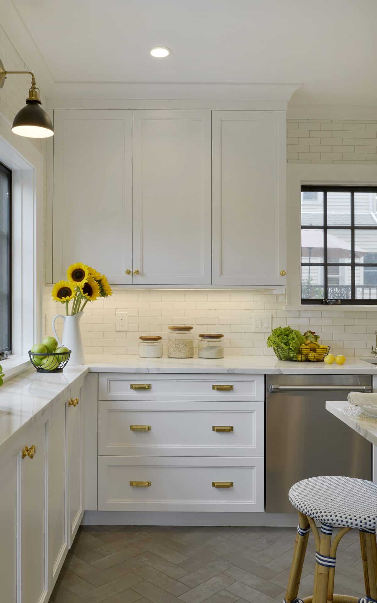 Classic kitchen features white cabinets, gold hardware and herringbone pattern floor.