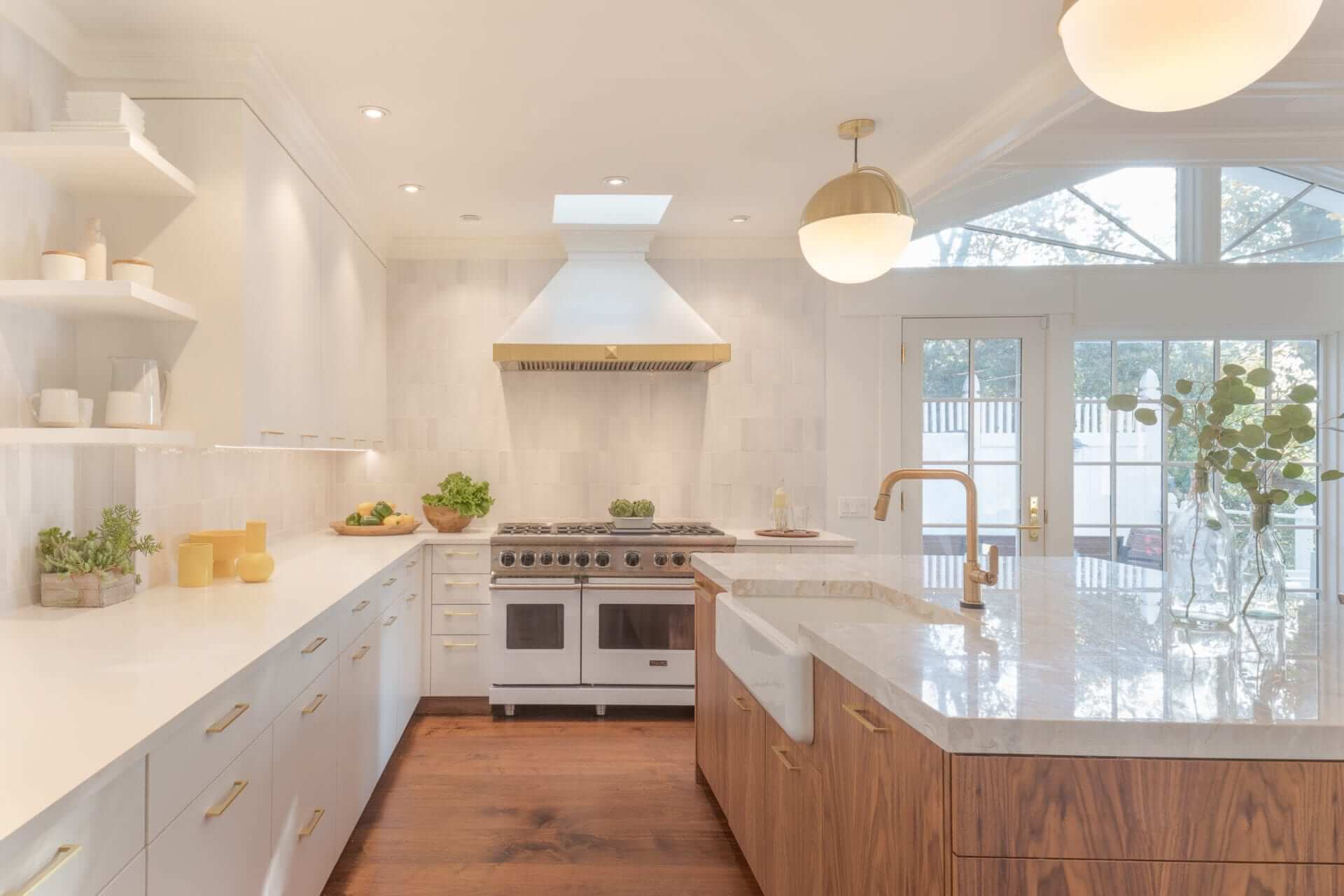 Contemporary kitchen features brass accents, white Rutt Regency cabinetry and white marble topped walnut island.