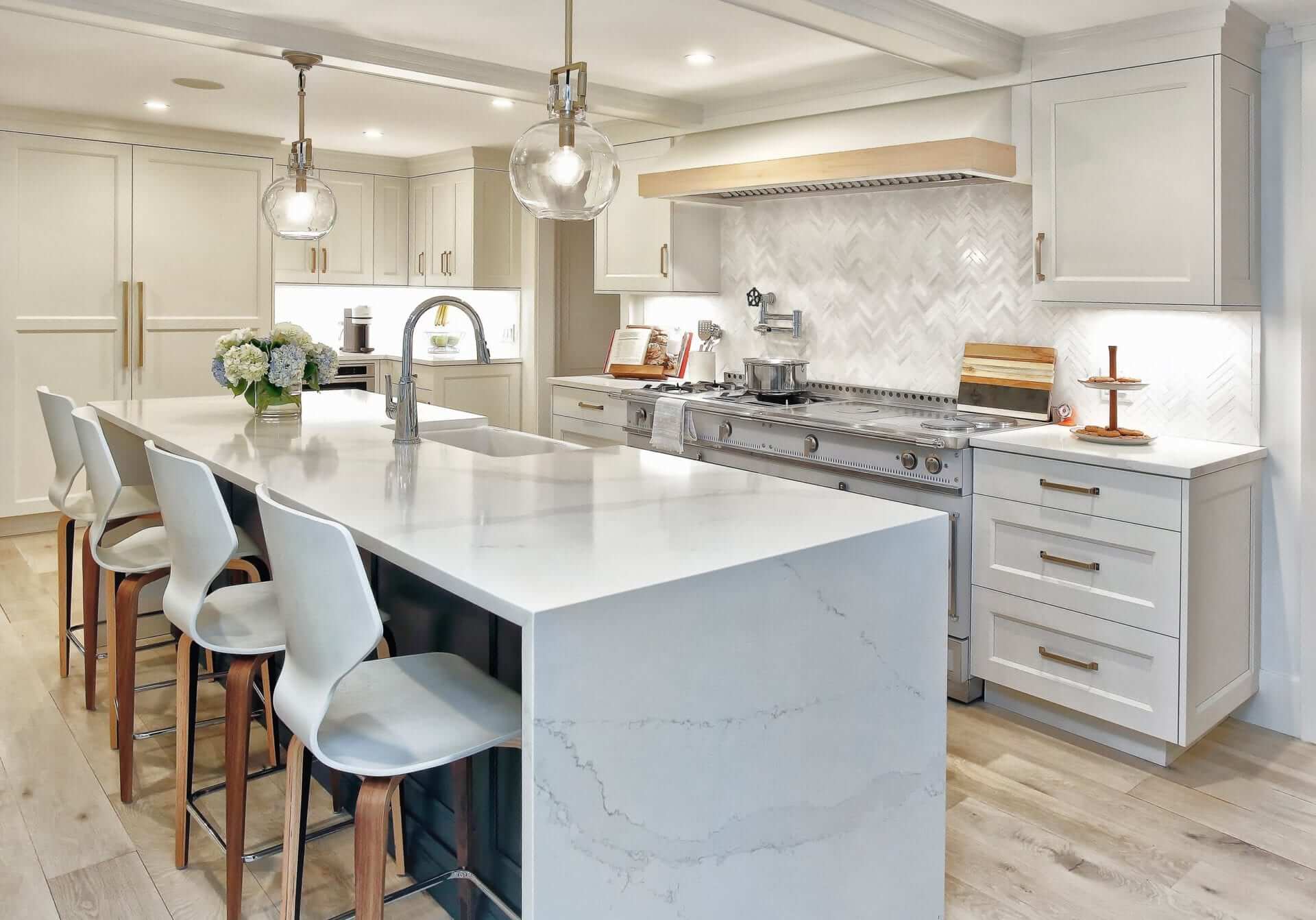 Kitchen features grey veined marble waterfall island, white custom NAC cabinetry, chevron tile backsplash & antique-inspired accents.