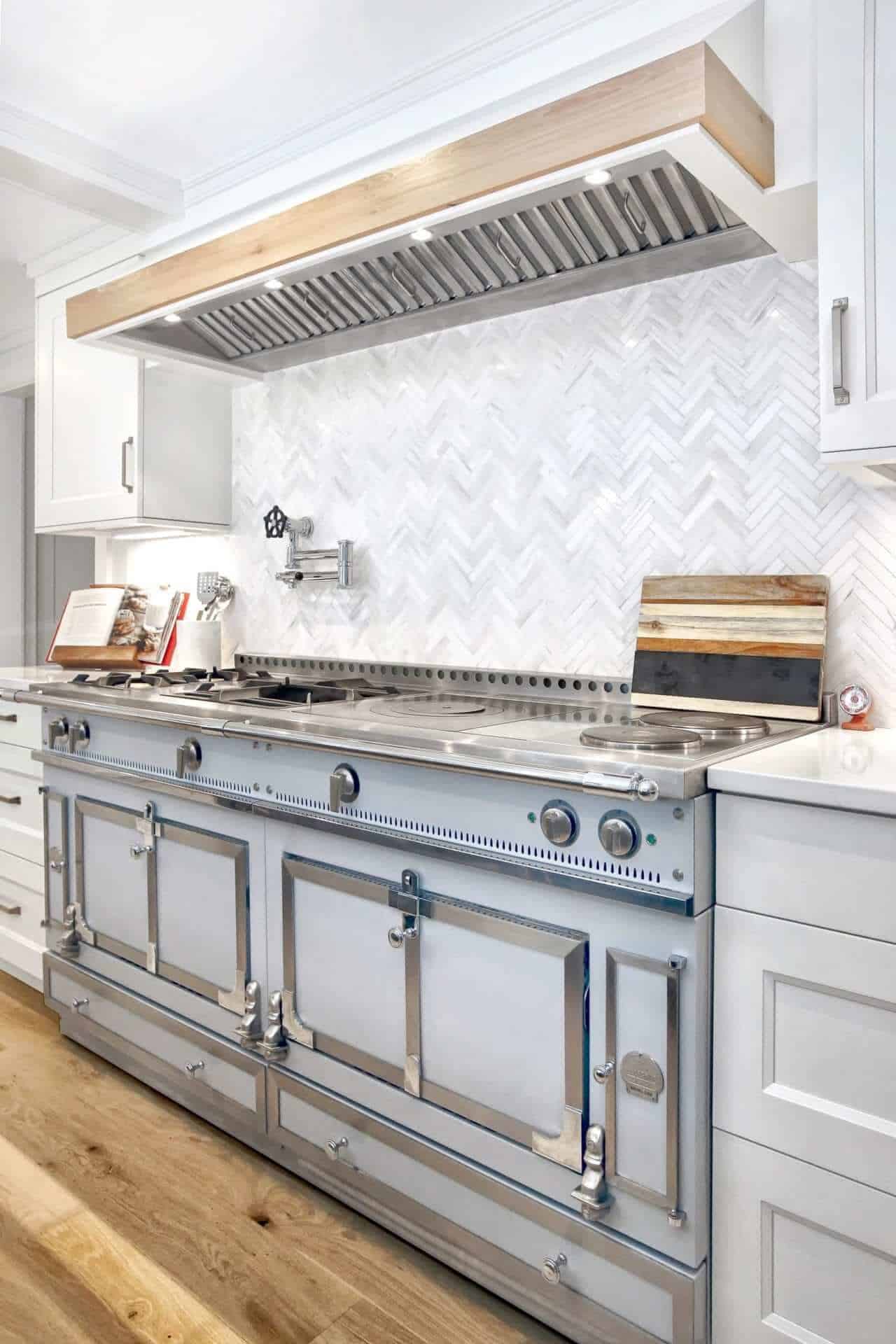 Antique-influenced kitchen features oversized La Cornue Range, chevron-patterned Waterworks tile backsplash and Dove White NAC cabinets.