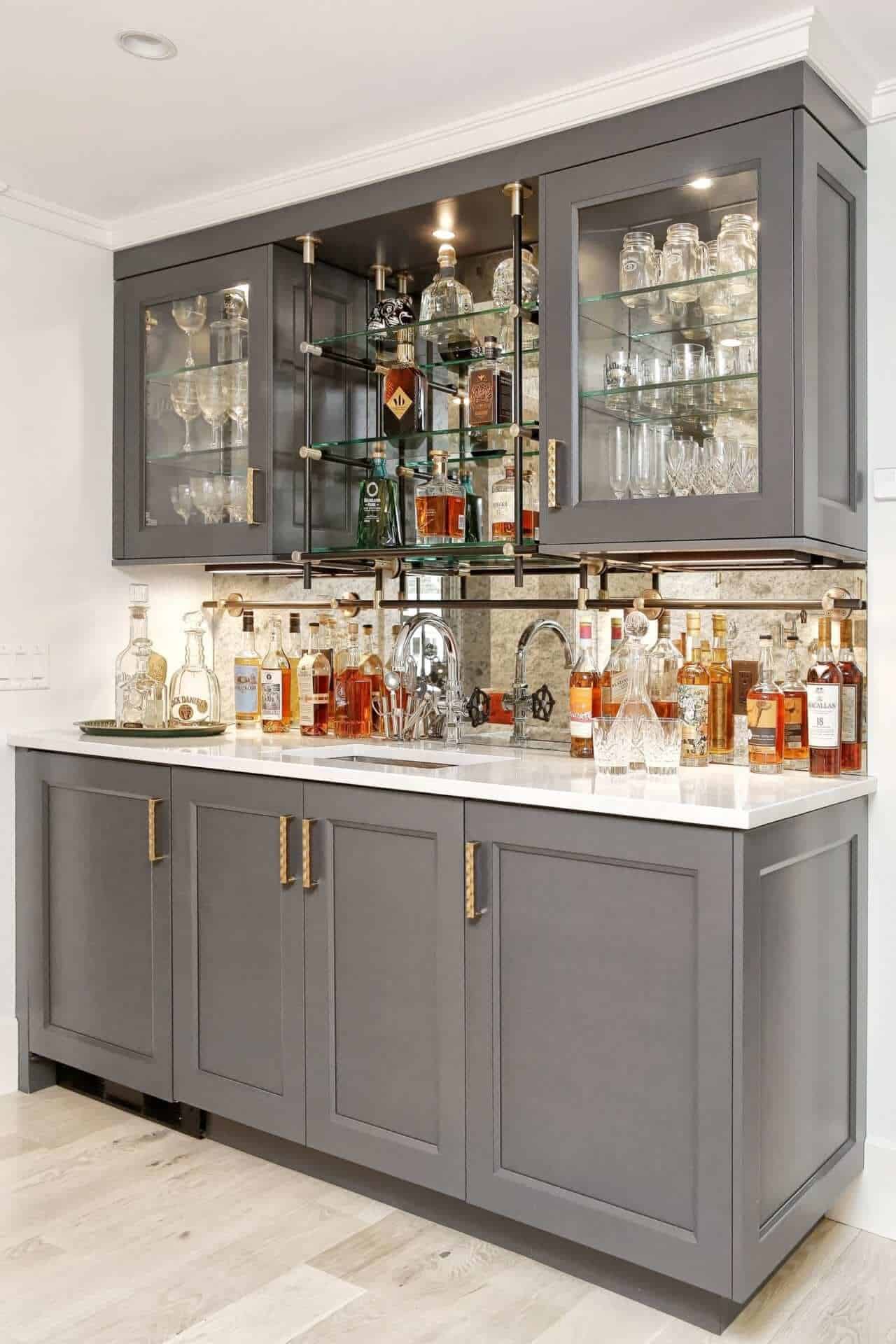 Custom vintage-inspired wet bar features Iron painted NAC cabinetry with brass hardware and antique mirrored backsplash.
