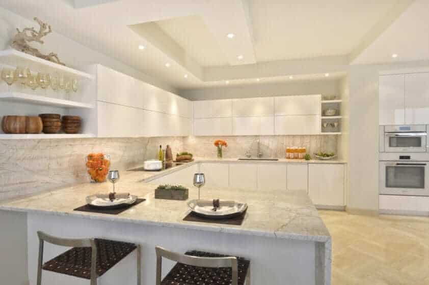 U-shaped tonal kitchen features white high-gloss Artcraft cabinets, Quartzite Bakaratta countertop with waterfall edge and light flooring.