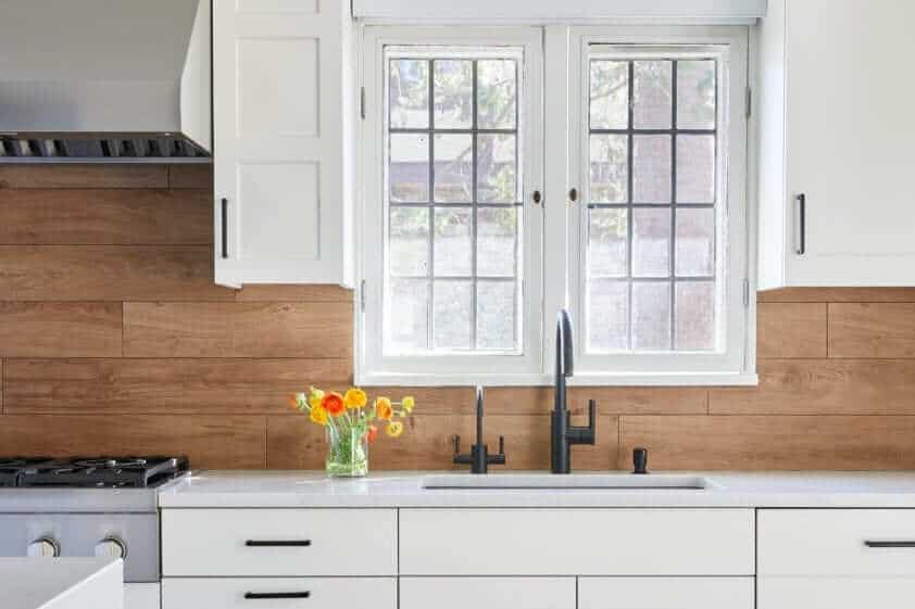 All white classic kitchen with wood backsplash and black faucet.