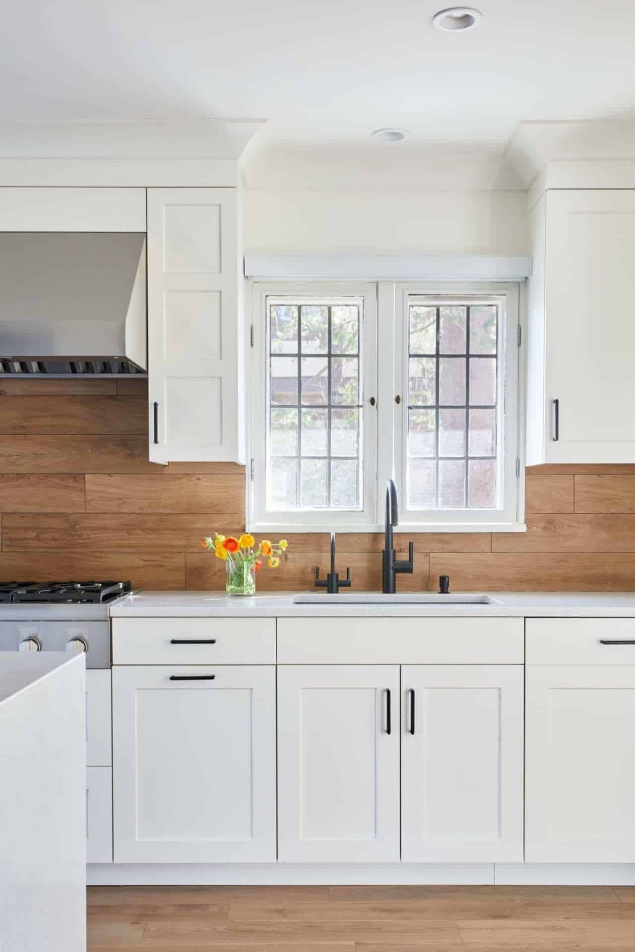All white classic kitchen with wood backsplash and black faucet.