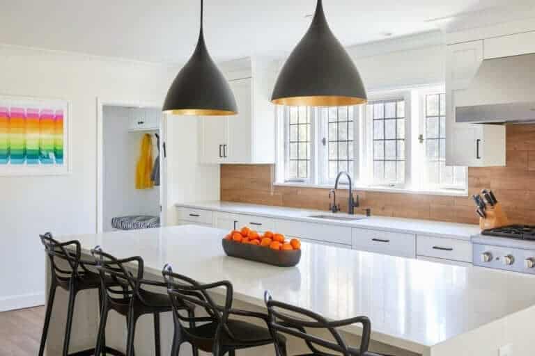 All white classic kitchen with wood backsplash and black and gold lighting above island.
