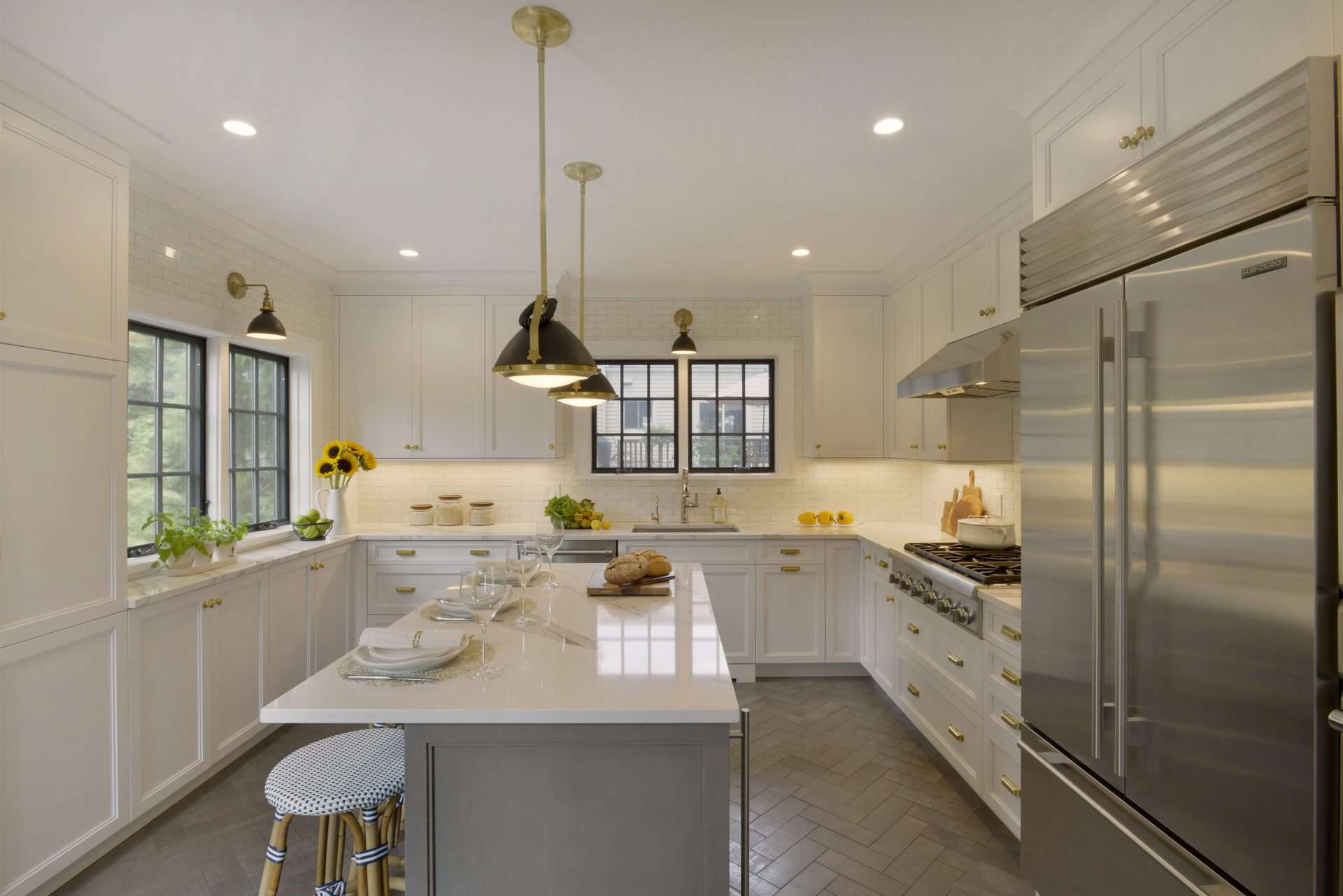 Mount Kisco Kitchen features white Caesarstone topped white NAC cabinetry, herringbone floor tile. and black and brass accents.