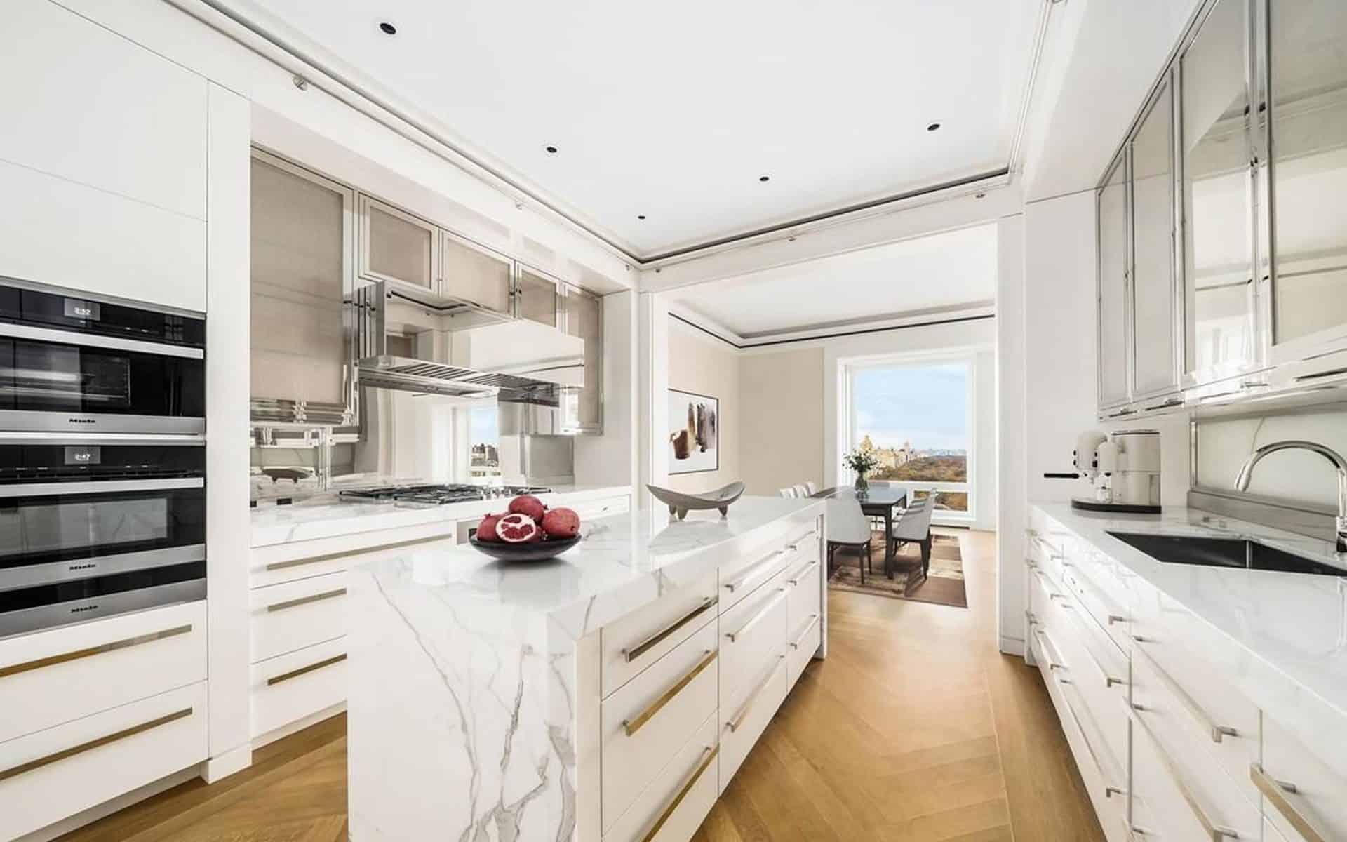 Sleek condominium kitchen features custom marble island, custom white cabinetry with chrome accents and glass front cabinets.