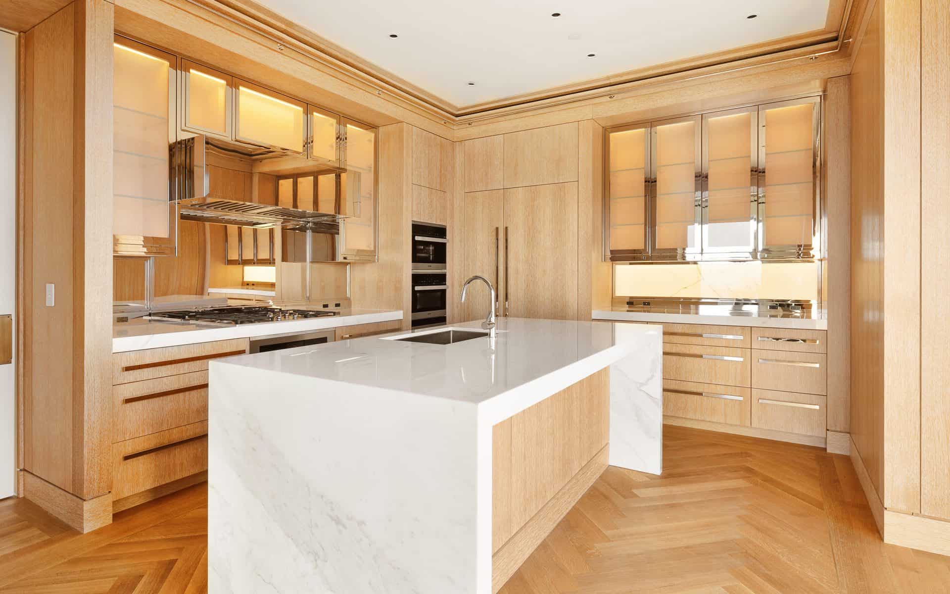 Modern condo kitchen features white marble waterfall island, custom light wood Bilotta cabinets and chrome accents