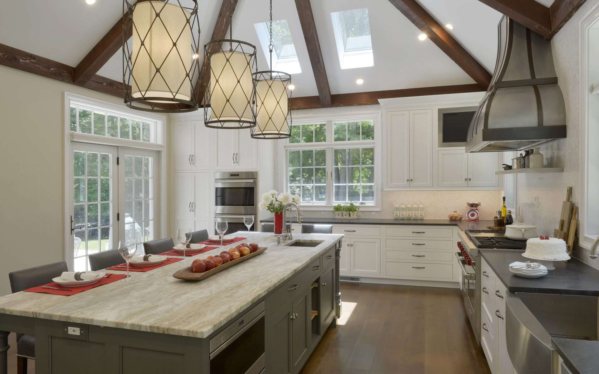 Elegant French-country style kitchen features gray custom island, dark wood beams and spacious sunlit windows.
