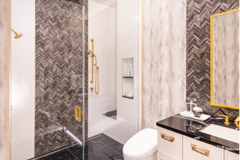 Modern bath with Bilotta cabinets, black marble floor and marble herringbone mosaic behind the sink and shower and brass accents.