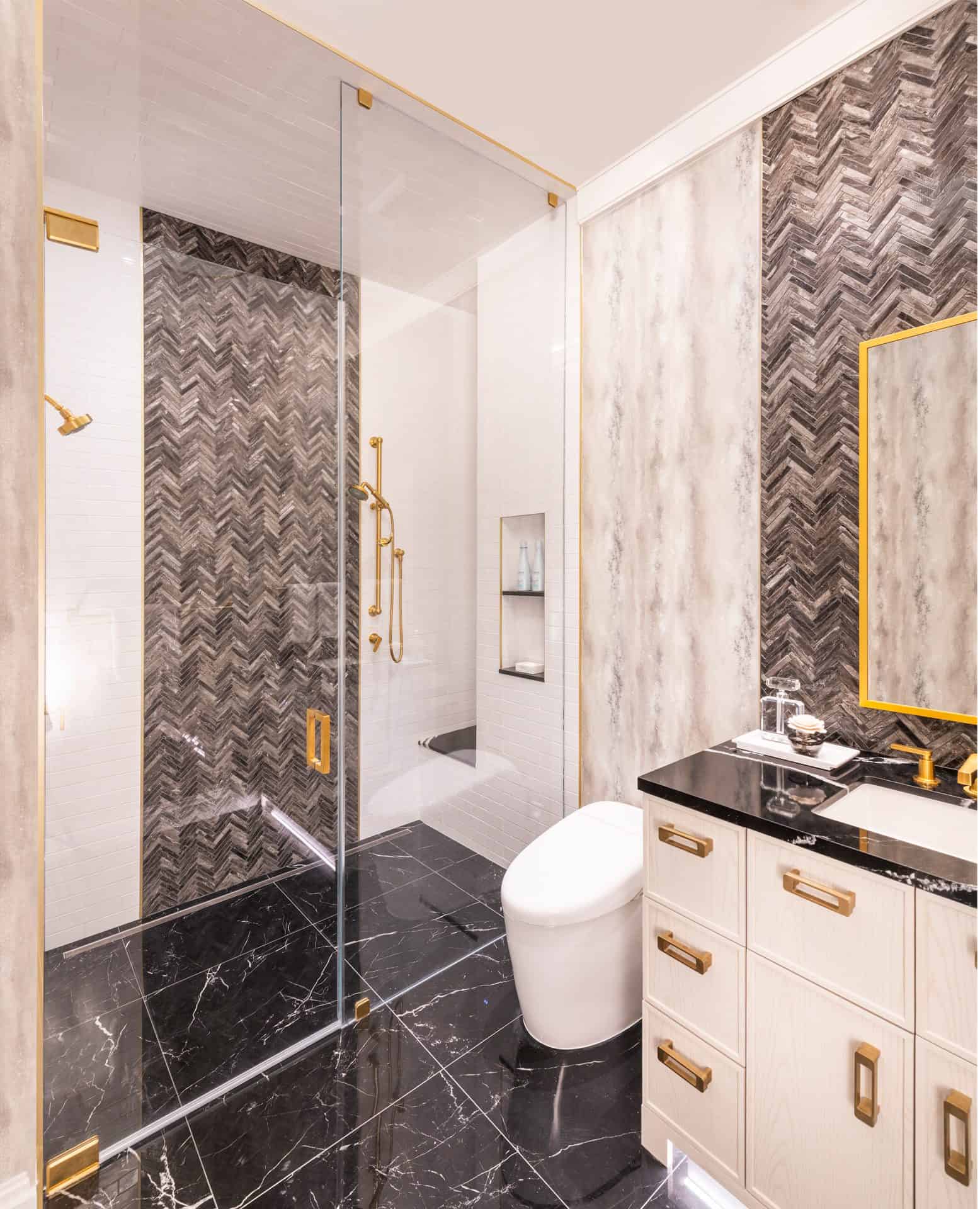 Modern bath with Bilotta cabinets, black marble floor and marble herringbone mosaic behind the sink and shower and brass accents.