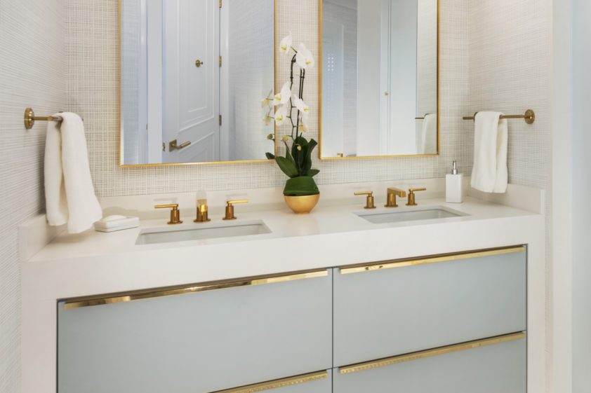 Luxury custom vanity features blue Bilotta cabinetry, high-end gold accents, and double lighted mirrors.
