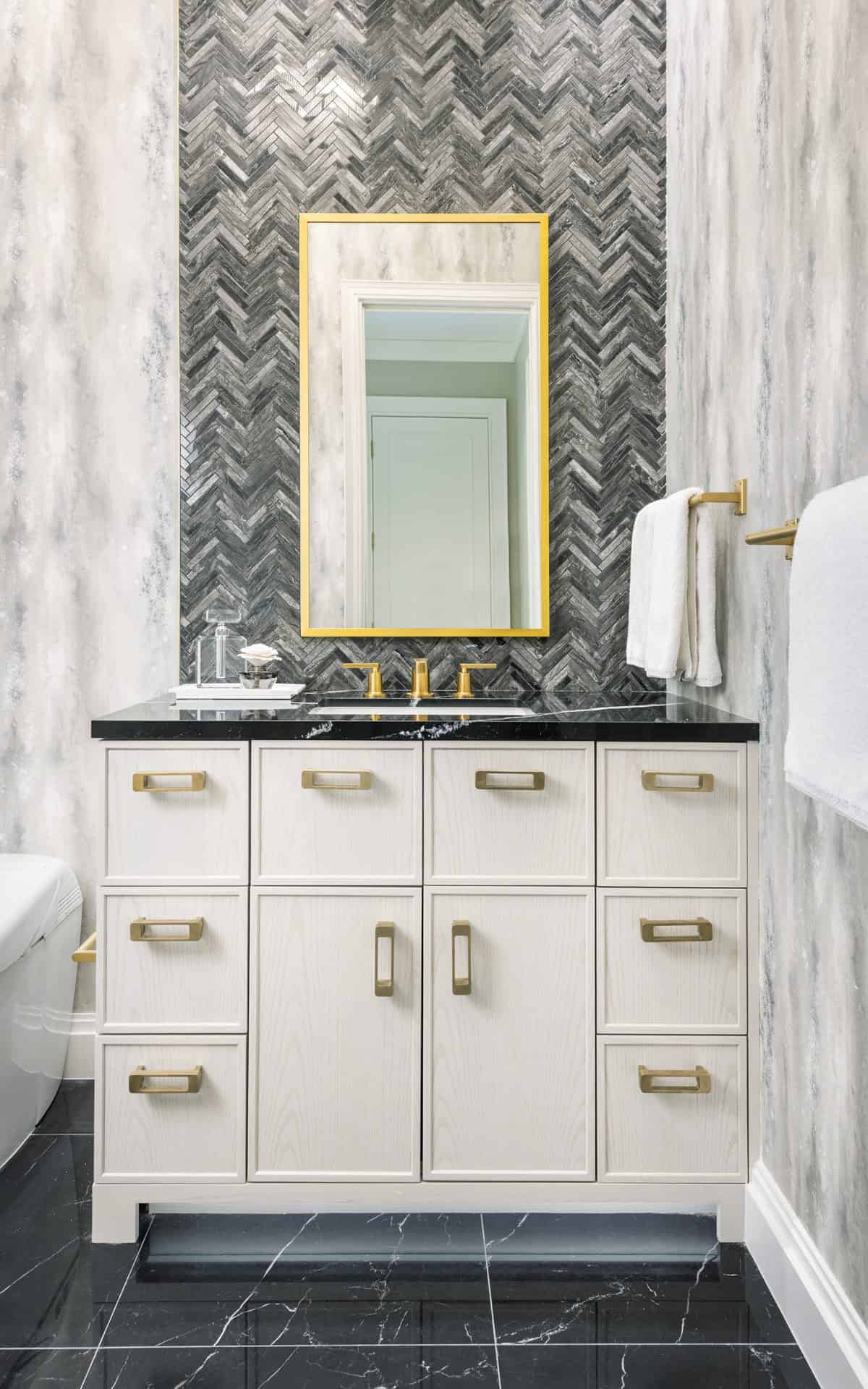Modern bath with Bilotta cabinets, black marble floor and marble herringbone mosaic behind the sink and brass accents.